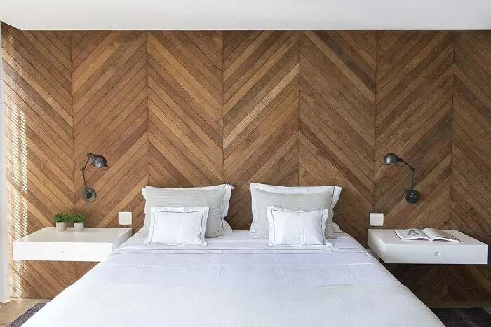 Quarto marrom: revestimento escama de peixe de madeira na parede e jogo de cama branco completa a decoração do espaço. Projeto de Triplex Arquitetura