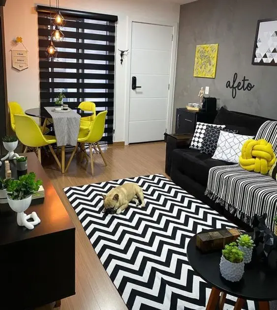 Sala com sofá preto, almofadas amarelas e tapete chevron