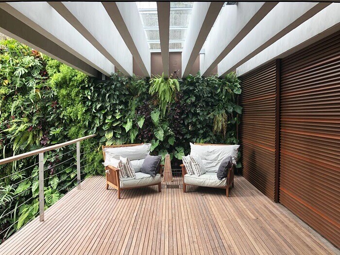 Sacada de madeira com jardim vertical e móveis rústicos com almofada
