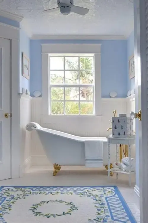Banheira de pé branca com dourado no banheiro decorado em azul