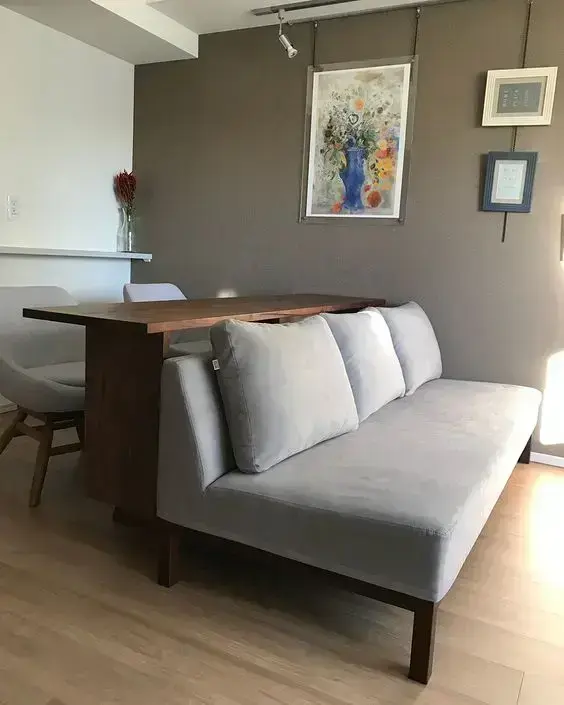 Home office na sala com sofá cinza e mesa de escritório de madeira
