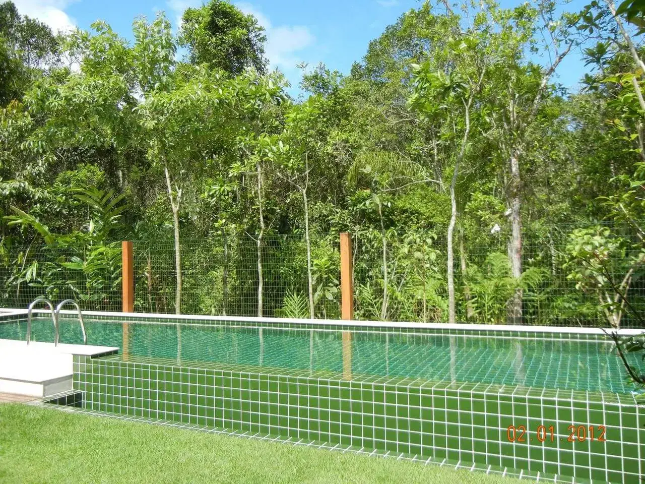 O azulejo de piscina verde se mistura a vegetação do terreno. Projeto de Olegário de Sá &amp; Gilberto Cioni