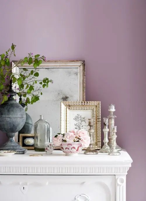 Parede de sala decorada na cor lilás com móveis brancos e quadros com moldura dourada