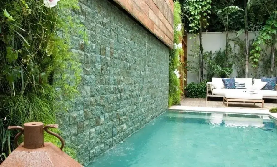 Piscina com azulejo verde e jardim vertical decoram a área externa do imóvel. Projeto de André Arquimagens