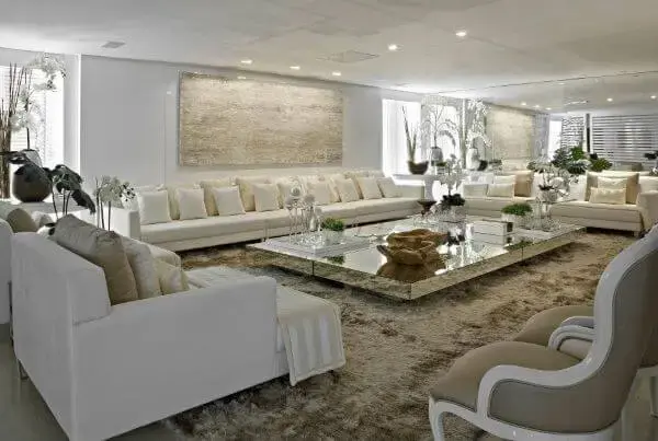 Sala grande decorada com sofás bege e mesa de centro espelhada