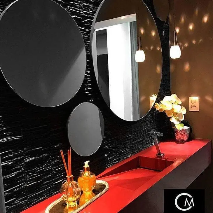 Banheiro com parede de filetes de ardósia preta, espelhos redondos e bancada vermelha 