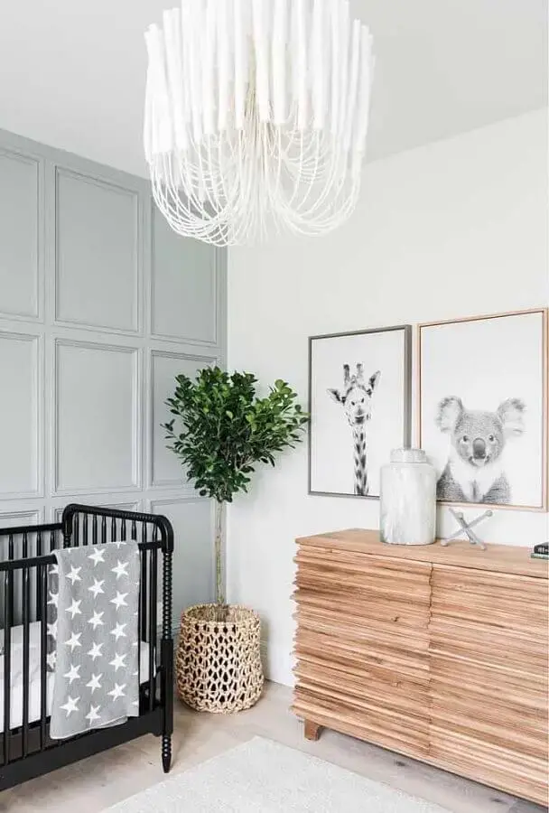 Cômoda de madeira para quarto de bebê decorado com berço preto e vaso de chão Foto No Decora