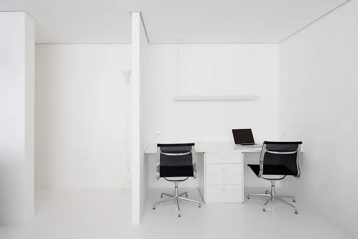 Escritório clean com cadeira preta e escrivaninha com gaveteiro branco. Projeto de Felipe Hess