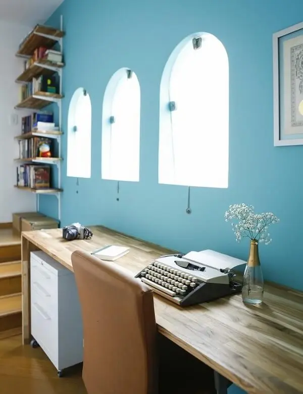 Home office com parede azul, escrivaninha de madeira e gaveteiro branco. Projeto de Buji Decoração Reuso