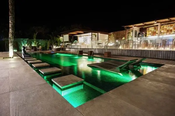 Piscinas modernas para casas grandes com iluminação verde dentro da piscina e espreguiçadeiras