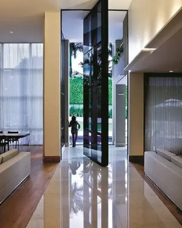 Porta gigante e cortinas brancas decoram o imóvel com pé direito duplo. Fonte: Revista Viva Decora 2