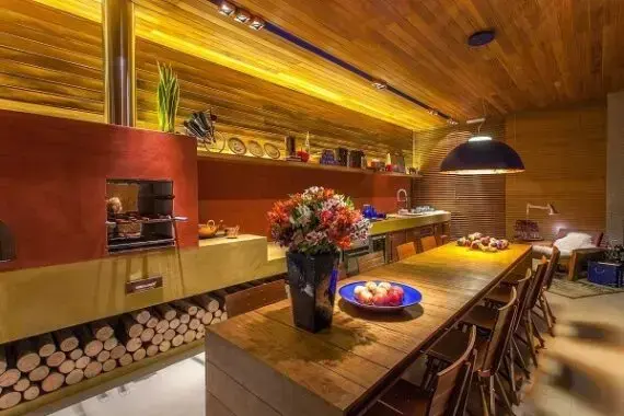 Área gourmet moderna com fogão a lenha e mesa de madeira grande
