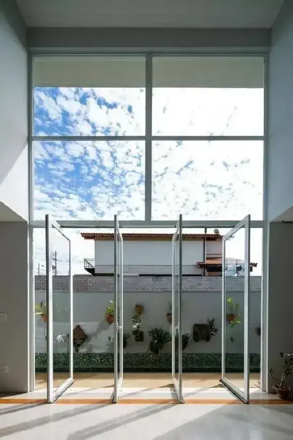 Porta para sala de vidro do tipo pivotante favorece a entrada de luz natural e ventilação no ambiente. Fonte: JAA Arquitetos
