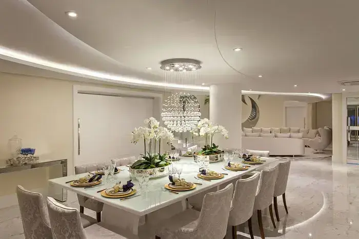 Sala de jantar grande de luxo com orquídeas e lustre de cristal. Fonte: Iara Kilaris