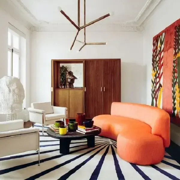 As poltronas brancas trazem a neutralidade necessária para a sala com sofá curvo laranja. Fonte: ELLE Decoration UK