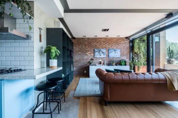Decoração de sala sem tv integrada com a cozinha e sofa marrom e papel de parede de tijolinho