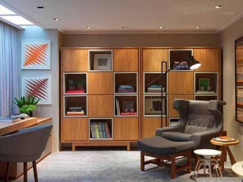 Escritório moderno decorado com poltrona cinza confortável e armário para colocar livros Foto Sergio Rodrigues