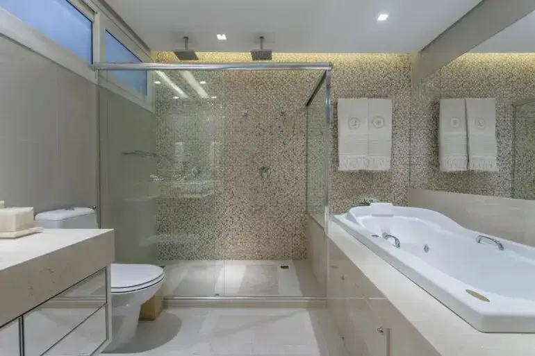 O espelho em cima da banheira simples de hidromassagem traz a sensação de amplitude no cômodo. Fonte: Vanja Maia