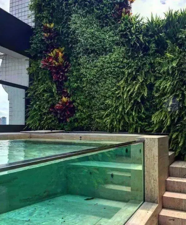 Piscina elevada de vidro com decoração de jardim vertical