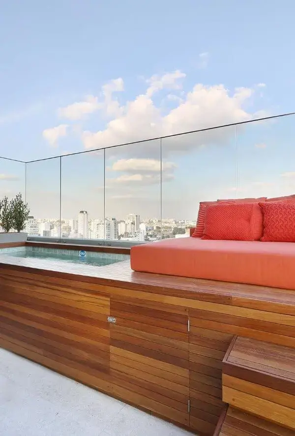 Quintal com piscina elevada e deck de madeira com sofá laranja