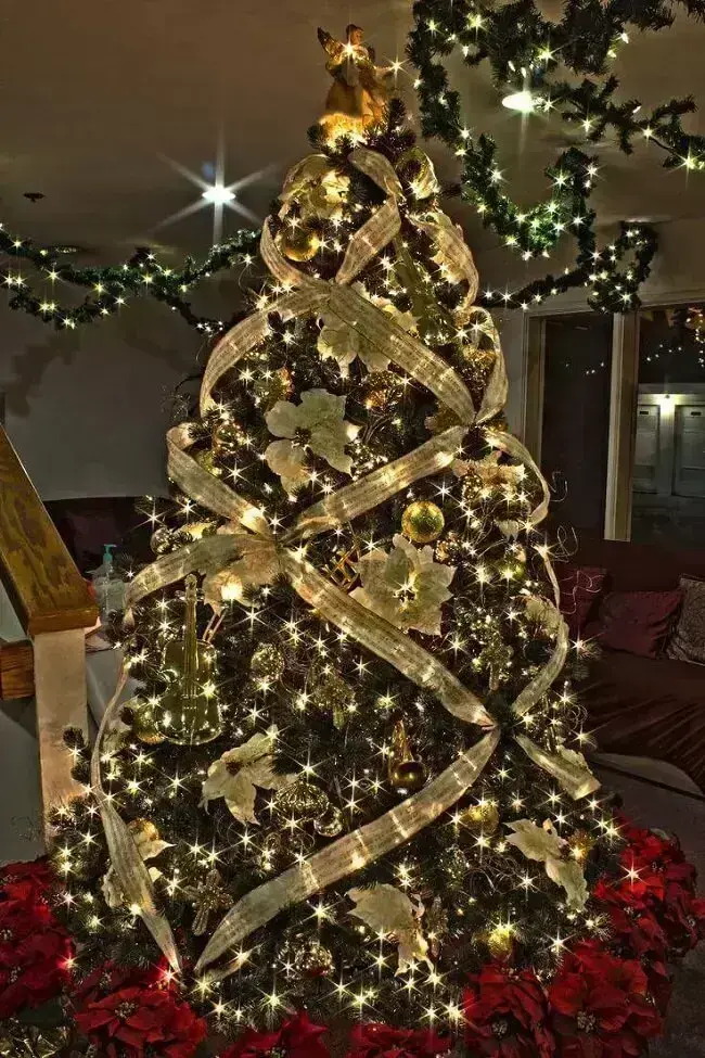 Árvore de natal dourada com decoração de fitas, flores e bolinhas. Fonte: 
