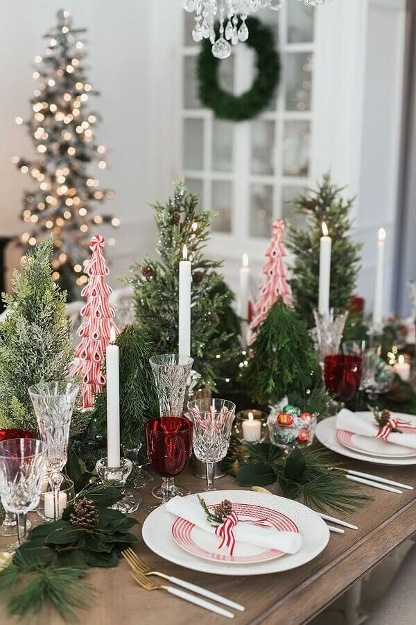 Arranjo de mesa para ceia natalina decorada com mini pinheiros e velas Foto Pizzazzerie