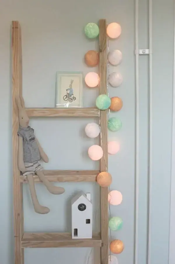 Escada para decoração de quarto de bebê enfeitada com cordão de luz e brinquedos. Fonte: Handy Little Me