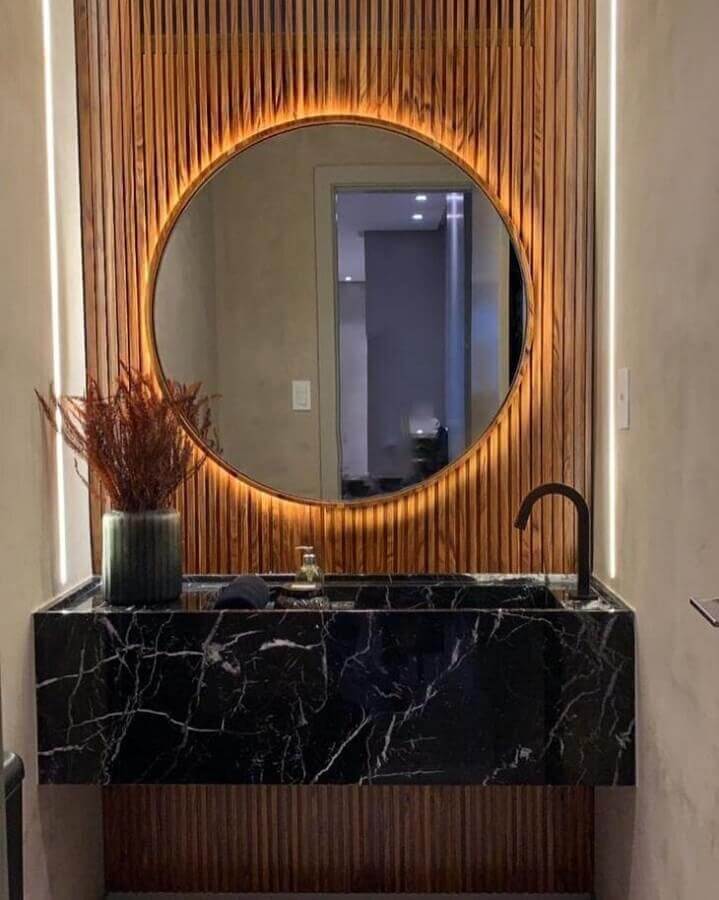 Parede ripada para banheiro pequeno decorado com espelho redondo e bancada de mármore preto Foto Romero Arquitetura