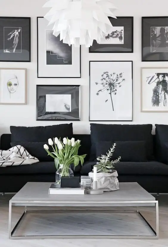 Sala branca com sofá preto e quadros variados em peb
