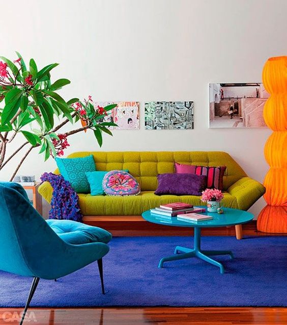 Sala colorida com sofá pé de palito verde e poltrona azul na mesma cor que o tapete