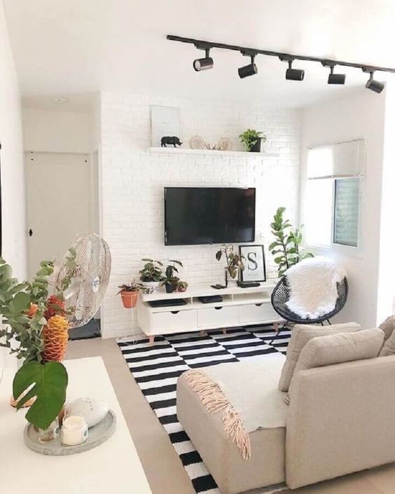 Sala preta e branca pequena com sofá bege e plantas no aparador