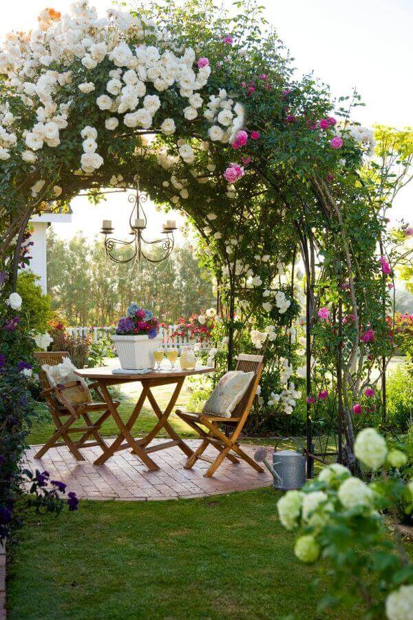 Jardim com pergolado e luminária de jardim acima da mesa de madeira
