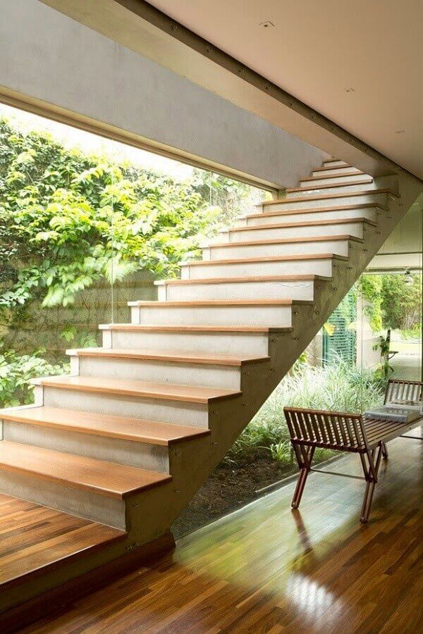Jardim embaixo da escada com banco de madeira e parede de vidro