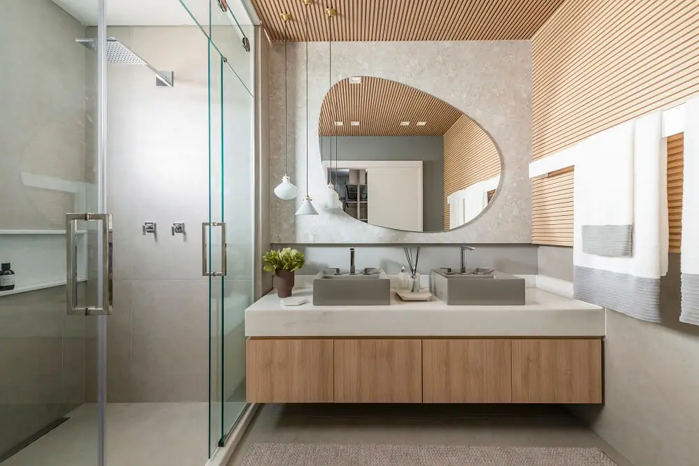 Banheiro da suíte master decorado com cubas de apoio e espelho em formato orgânico. Projeto de Bohrer Arquitetos