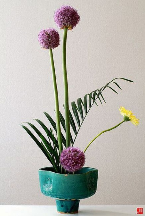 Ikebana delicada com vaso azul e flores em roxo e amarelo