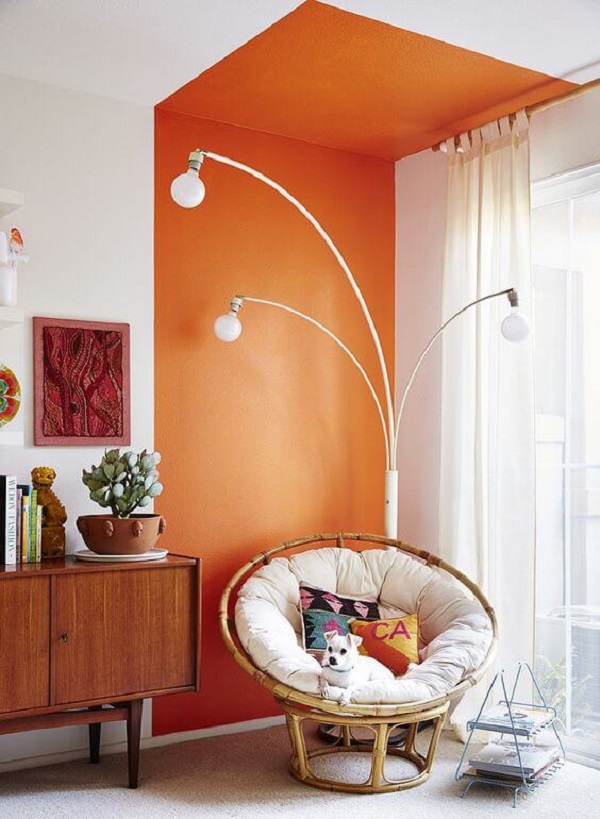 Parede de sala decorada com pintura setorizada laranja perto do rack minimalista e poltrona de ratan