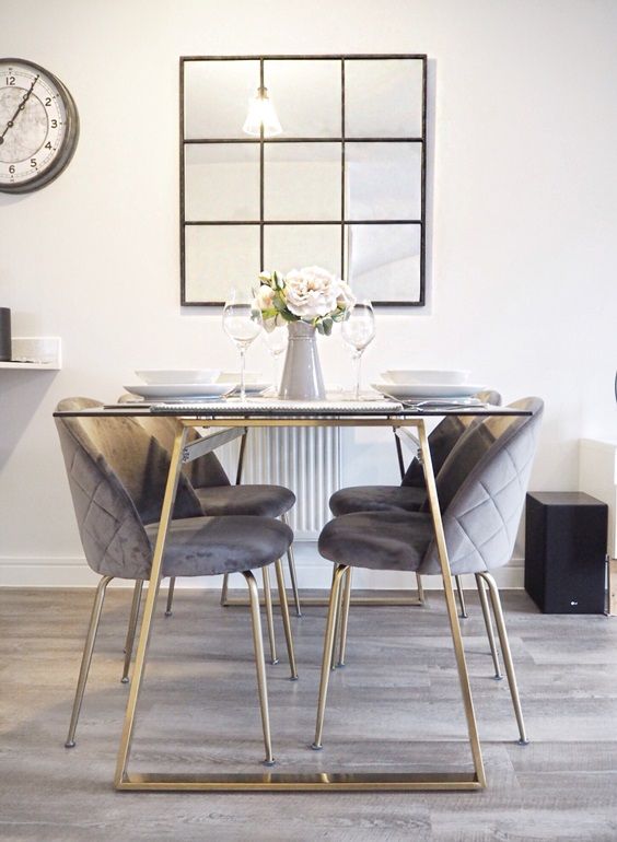 Base para mesa de jantar dourada com tampo de vidro e cadeiras cinza