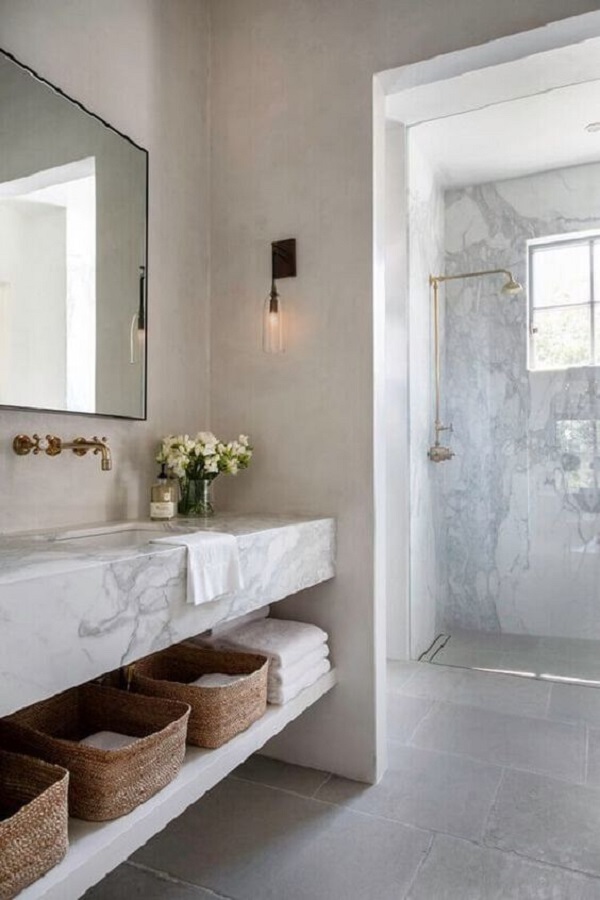 Banheiro com pia de mármore branco e torneira de parede dourada