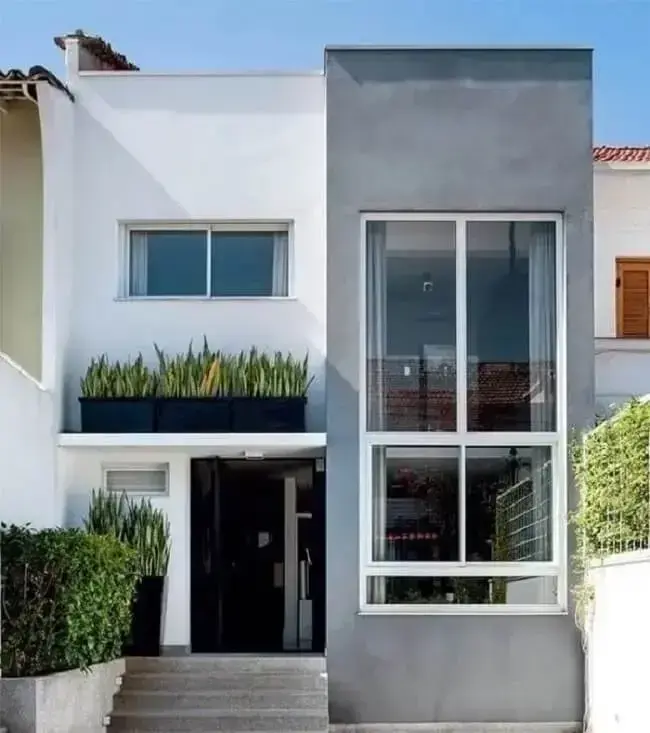 Grandes aberturas favorecem a iluminação natural da casa sobrado com fachada cinza e branco