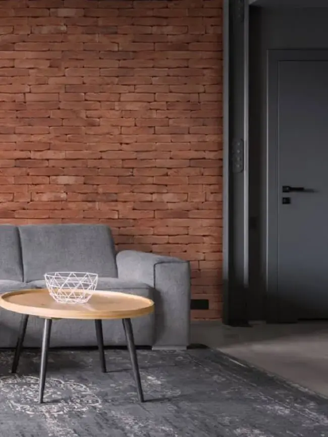 Sofá cinza e parede de tijolo de demolição decoram a sala de estar. Fonte: Mattone Di Venezia