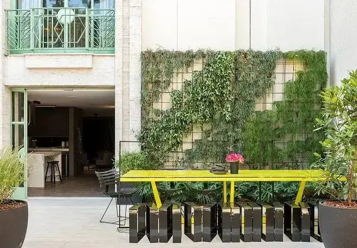 Área de lazer com mesa de madeira amarela e jardim vertical externo. Fonte: Studio Clariça Lima
