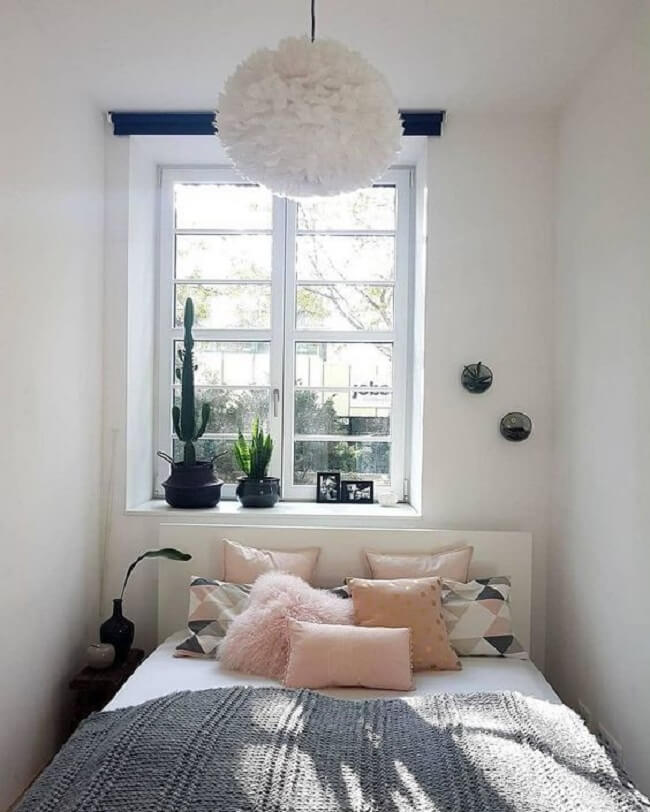 Almofadas em tom rosa decoram a cama embaixo da janela