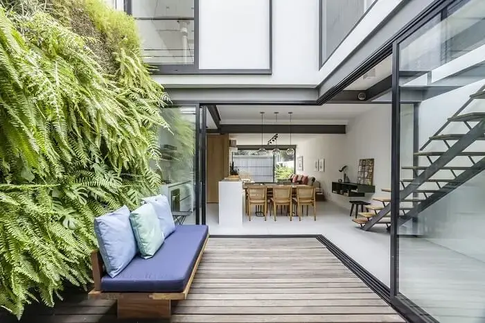 Deck de madeira, sofá azul e parede de plantas