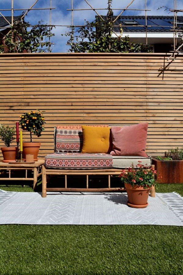 Área externa com tapete, vasos de plantas e sofá de bambu