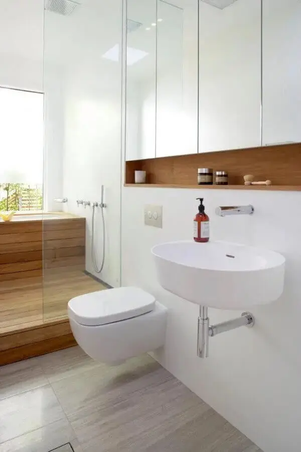 Banheiro branco com área de banho em madeira e chuveiro de teto