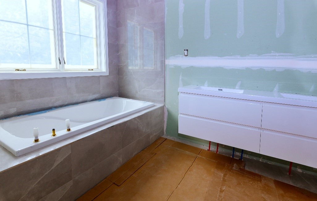 Banheiro em construção com paredes de drywall rosa e verde e uma banheira de hidromassagem.