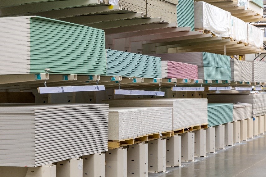 Depósito com placas de drywall das cores rosa, branca de verde, empilhadas e organizadas
