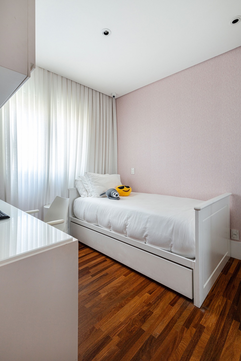 O papel de parede rosa claro traz um toque delicado para o quarto de menina