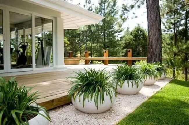 Ao lado do deck vasos e pedra branca para jardim decoram o espaço
