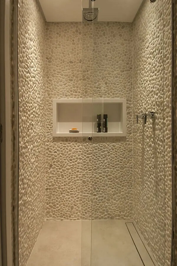 Banheiro com parede revestida de seixos e ralo linear oculto